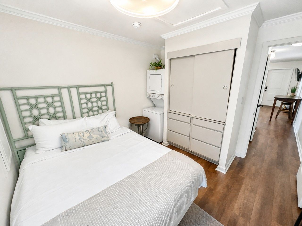 Un dormitorio con cama, armario, mesita y espejo.