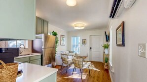 A compact kitchen with modern appliances, a dining area with a wooden table and chairs, and a hallway with a door and wall-mounted decor. - Picture book cottage! (Ocean Springs)