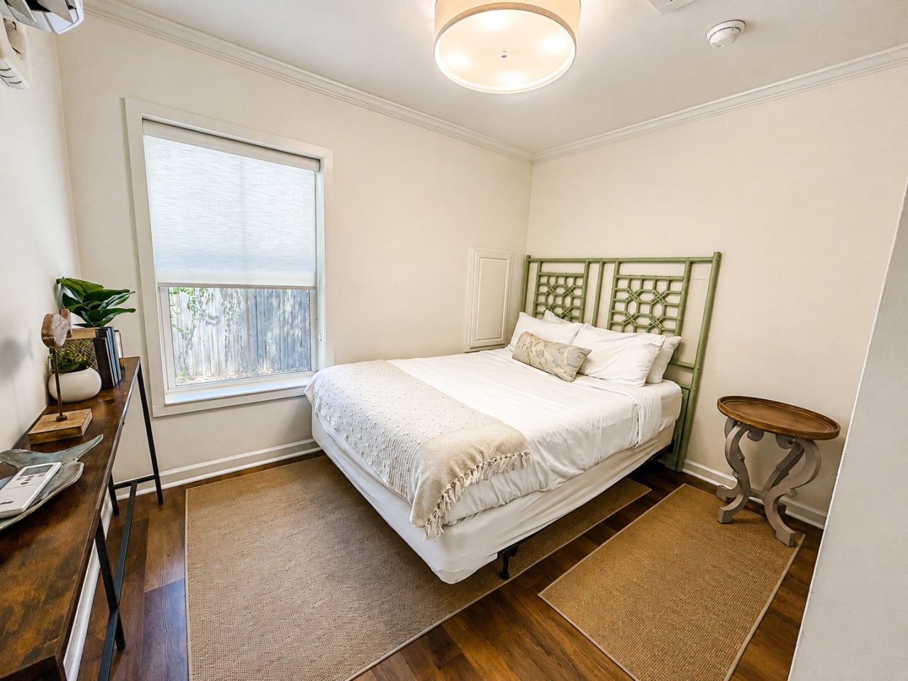 A bedroom with a bed, a window, a bedside table, and a small table with a lamp.