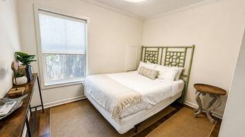 A bedroom with a bed, a window, a bedside table, and a small table with a lamp.