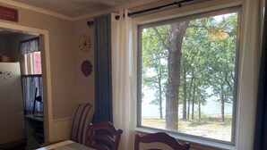 A dining area with a table and chairs, a window with a view of trees, and a red basket on the table. - Eufaula Lake front access w/wraparound deck and spectacular views! Pet friendly! (Checotah)