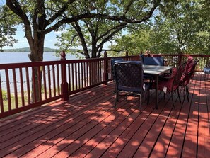 Une terrasse en bois avec une table et des chaises, donnant sur une étendue d’eau.