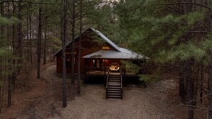 A cabin surrounded by dense forest, with a wooden deck and a staircase leading to the entrance. - Romantic|Private|Wellness|OutdoorMovieNight (Broken Bow)