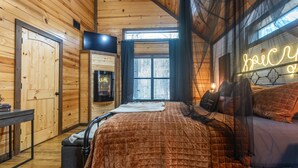 A cozy wooden cabin bedroom with a bed, a desk, and a neon sign. - Romantic|Private|Wellness|OutdoorMovieNight (Broken Bow)