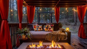 A cozy outdoor seating area with a fire pit, a cushioned bench, and a hanging chair. - Romantic|Private|Wellness|OutdoorMovieNight (Broken Bow)