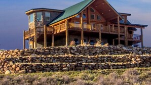 Une grande cabane en bois à plusieurs étages, dotée de fondations en pierre, de nombreux balcons et d’un toit végétalisé.