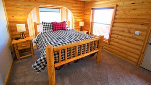Une chambre dans une cabane en bois, avec un lit, deux tables de chevet et une fenêtre.