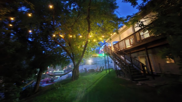 A tree-lined pathway leading to a building with a staircase and a balcony.