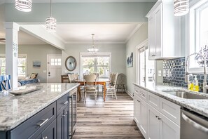 A kitchen with granite countertops, white cabinets, and a dining area with a wooden table and chairs. -  6 BR/6 Ba w/ Pool & Hot Tub, ample Parking, close to Beach & Downtown! (Carolina Beach)