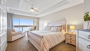 Une chambre à coucher avec un grand lit, une table de chevet, une commode, une chaise et un ventilateur de plafond.
