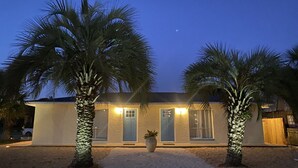 A two-story building with a flat roof, a front door, and a large window. There are two palm trees in front of the building.