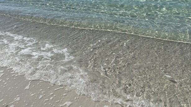 A beach with clear shallow waters and a sandy shore.