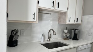 A modern kitchen with white cabinets, a stainless steel sink, and a coffee maker.
