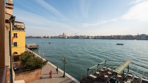 A waterfront view with a row of tables and chairs under a pergola, a clear sky, and a distant cityscape. - Ve.N.I.Ce. Cera Tintoretto Suite (Venezia)