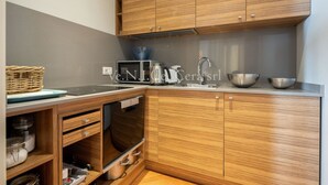 A modern kitchen with wooden cabinets, a microwave, a kettle, and stainless steel bowls.