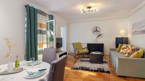 A living room with a sofa, a coffee table, a TV, and a dining area with a table set for two. - Holiday apartment Beach apartment Petra (Pula)