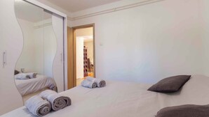 A bedroom with a bed, a large mirror, and a wardrobe. There are towels on the bed and a door leading to a hallway. - Holiday apartment Beach apartment Petra (Pula)