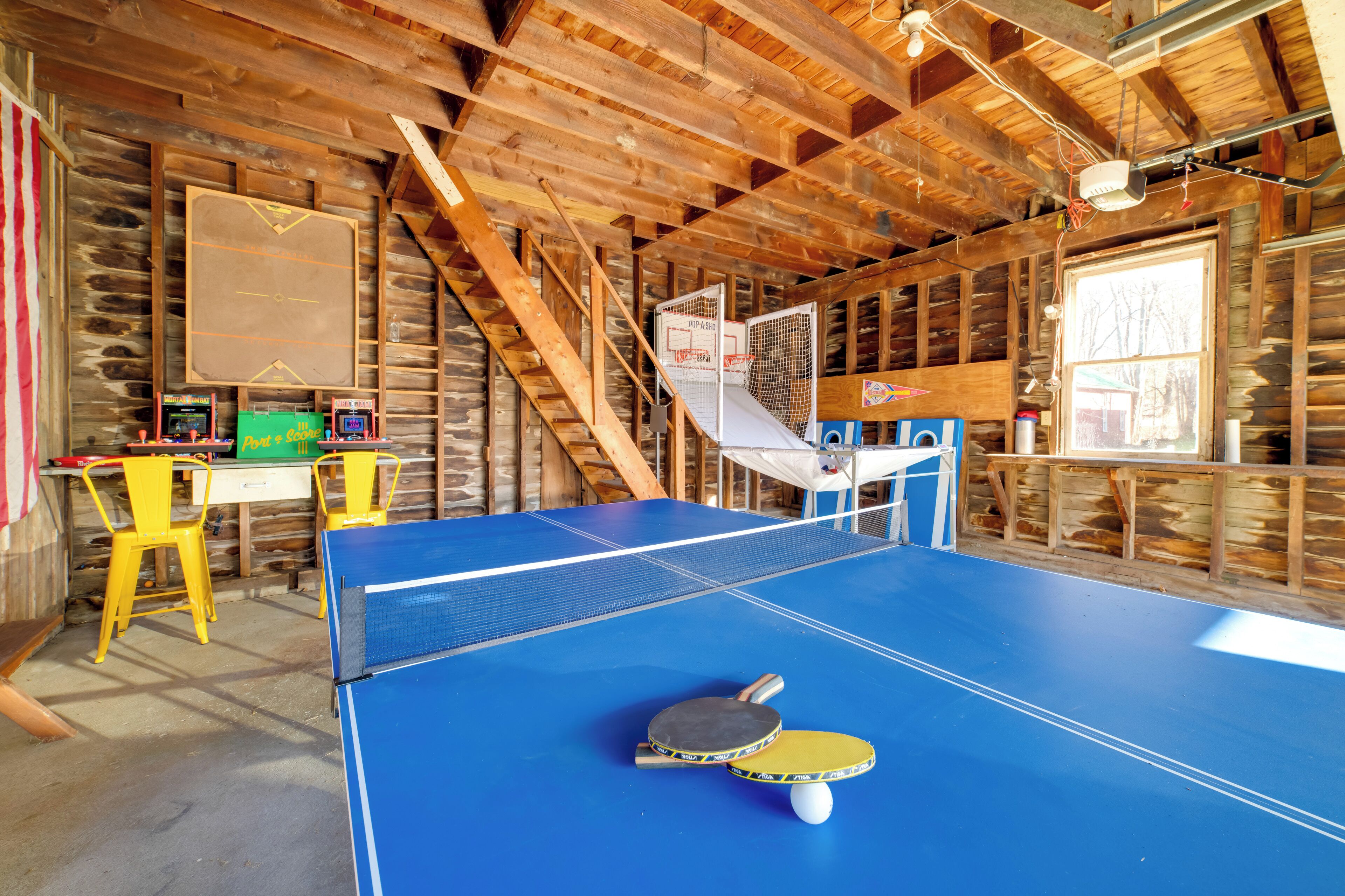 Una mesa de ping pong con dos paletas y una pelota, una escalera de madera y una pared de madera con una ventana.