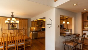 Een moderne keuken met houten kastjes, een eethoek met een houten tafel en stoelen, en een klein barretje met krukken.