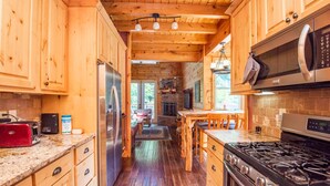 Een houten keuken in cottage-stijl met een stenen open haard, houten kastjes, een roestvrijstalen koelkast, een gasfornuis en een magnetron.