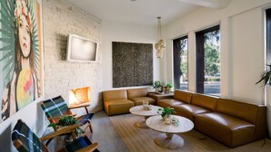 Un salon moderne avec un canapé d’angle, deux petites tables rondes et un grand tableau abstrait accroché au mur.