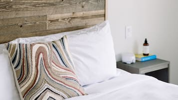 Un lit avec une tête de lit en bois, un coussin à motifs, une table de chevet avec une lampe et une bouteille d’eau.