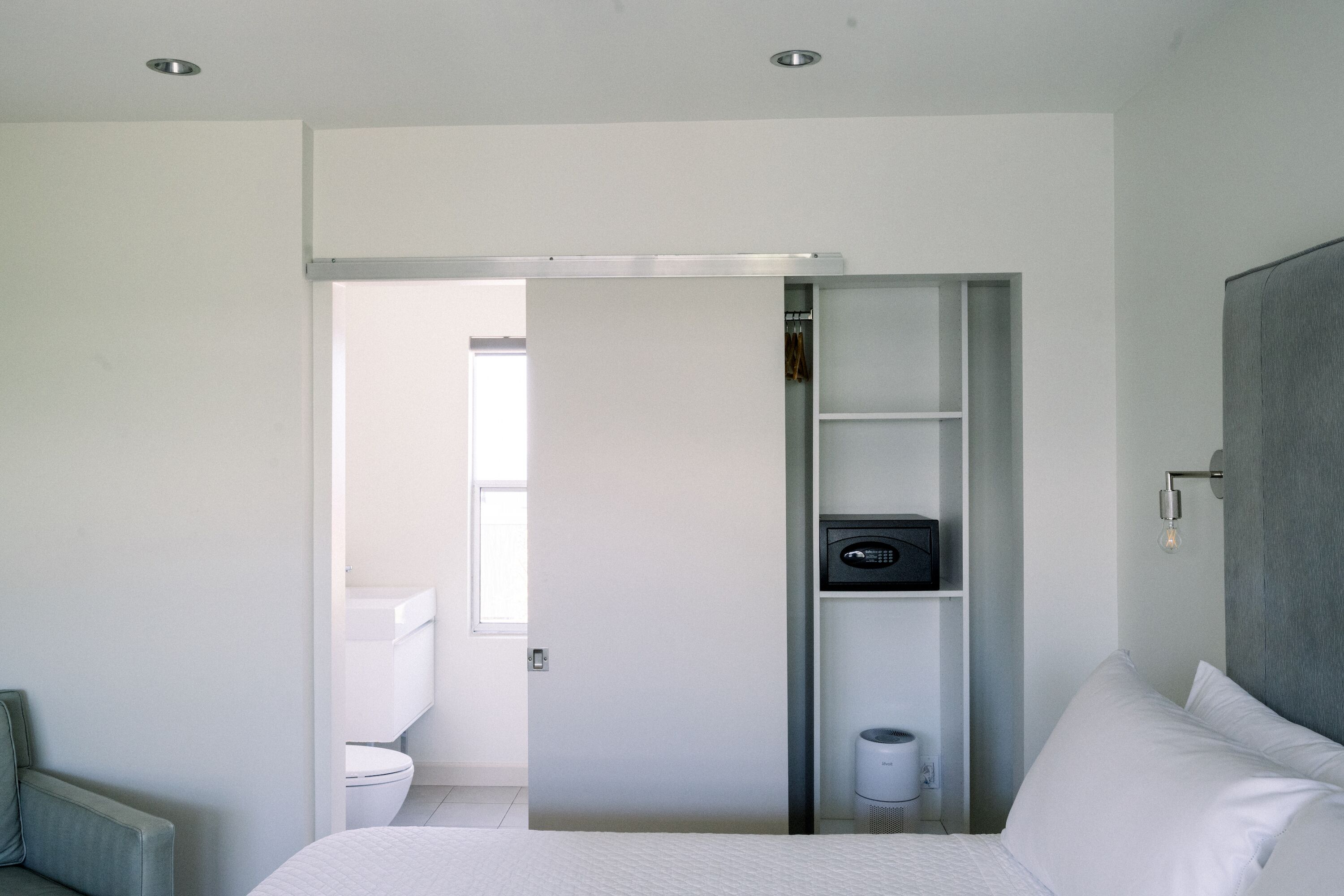 Quarto moderno com cama, guarda-roupa e casa de banho visível através de uma porta aberta.