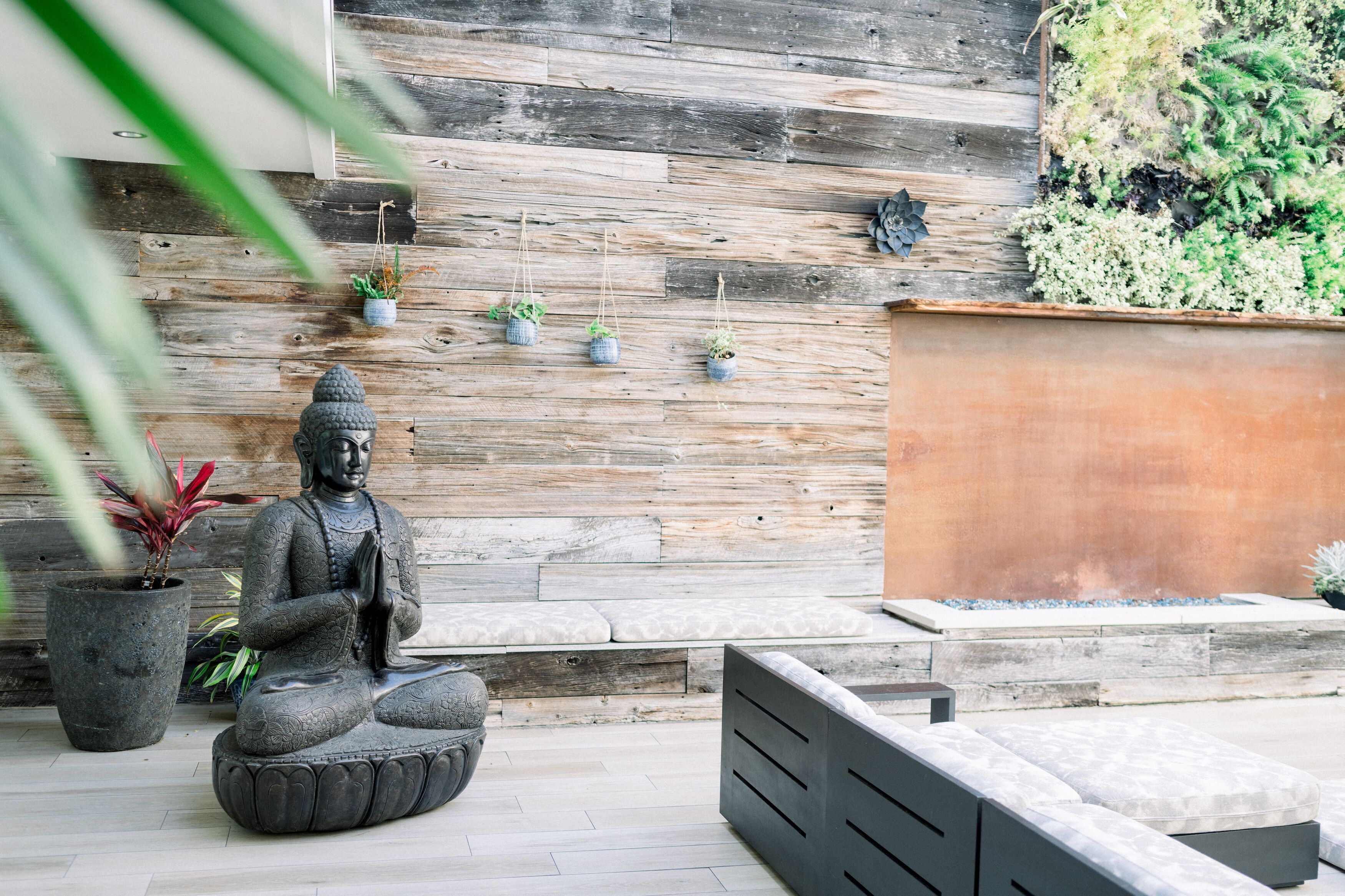 A statue of a seated figure, a wooden wall with hanging planters, and a seating area with cushions.