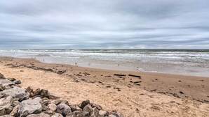 Uma praia com pedras em primeiro plano e ondas ao fundo.