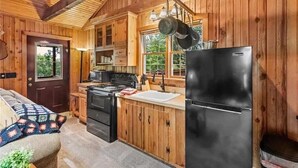 L’intérieur d’une cabane en bois comprend une cuisine équipée d’un réfrigérateur noir, de meubles de rangement en bois et d’une cuisinière.