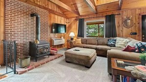 L’intérieur d’un chalet chaleureux, avec un mur en briques, un poêle à bois, un canapé et une tête de cerf accrochée au mur.