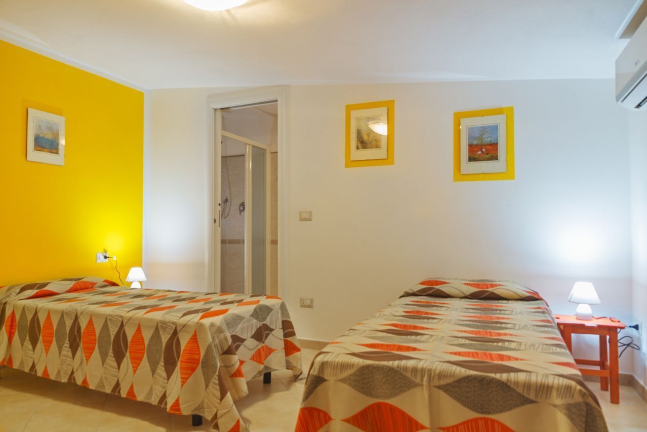 Habitación de hotel con dos camas, una puerta que da a un baño y dos cuadros en la pared.