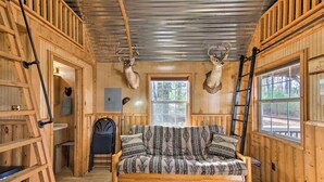 A wooden cabin interior with a sofa bed, a ladder, and two mounted deer heads. - Lakefront Cabin w/ 2 Lofts, Boats on 4 Acres (Winnsboro)