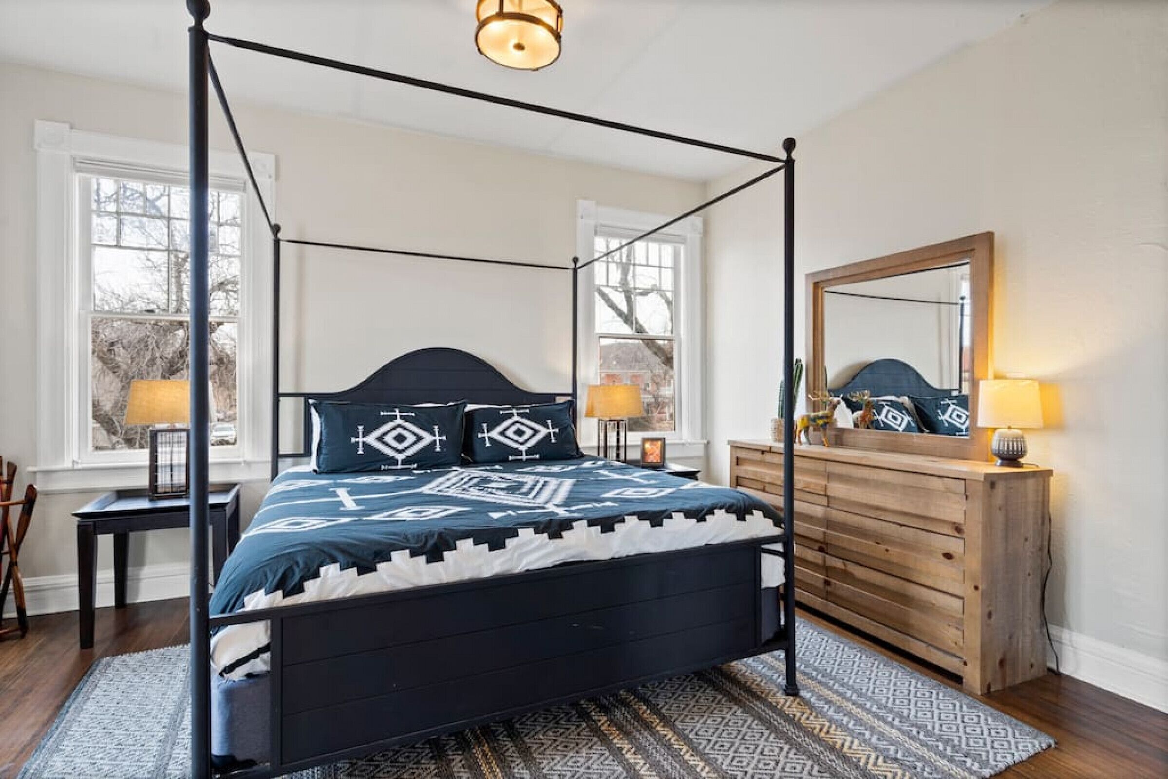 Un letto a baldacchino con una coperta a motivi geometrici, un comò in legno e uno specchio appeso al muro.