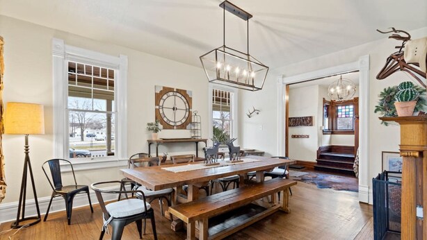 A spacious dining area with a wooden table and benches, large windows, and a chandelier. - The Pendleton Lodge-8 bedrooms/3baths-heart of COS (Colorado Springs)