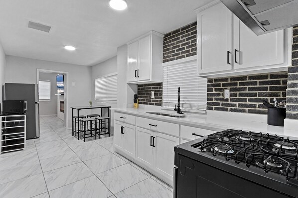 A modern kitchen with white cabinets, a gas stove, and a brick accent wall.