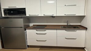 Une cuisine moderne avec des armoires blanches, un four encastré, un réfrigérateur en acier inoxydable et un plan de travail en bois.
