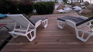 Deux fauteuils de jardin blancs avec des coussins noirs, placés sur une terrasse en bois.