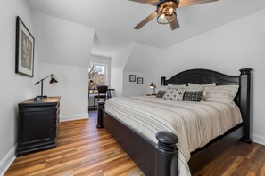 A bedroom with a large bed, a ceiling fan, a nightstand, and a desk.