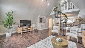 A spacious living room with a large TV, comfortable seating, a staircase, and a decorative chandelier. - A-Frame Cabin w/ Hot Tub: 5 Mi to Waterford! (Melrose)