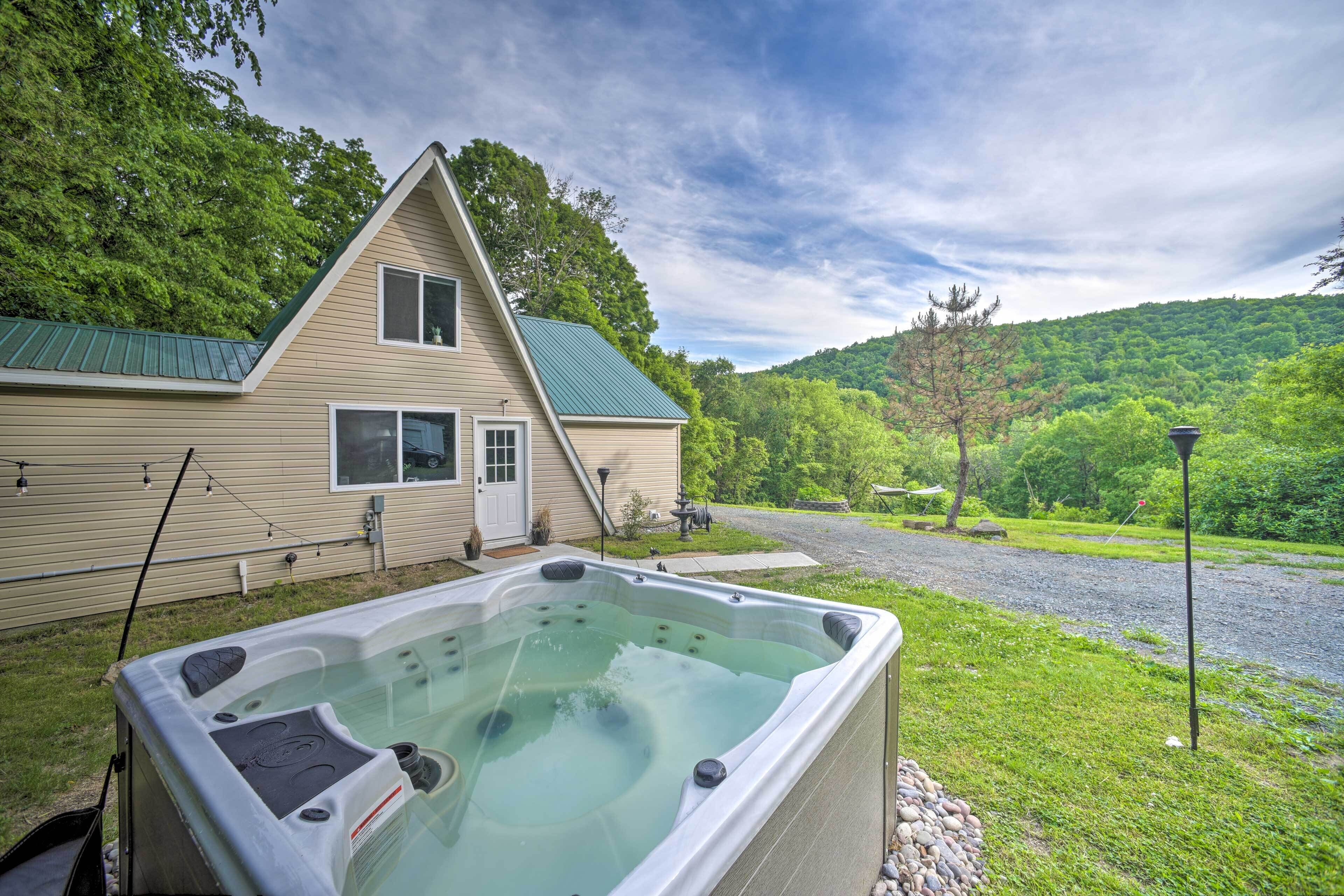 Ein Haus mit Whirlpool im Vordergrund, umgeben von viel Grün und einer Hügelkulisse.