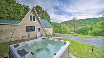 Ein Haus mit Whirlpool im Vordergrund, umgeben von viel Grün und einer Hügelkulisse.