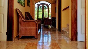 A hallway with a tiled floor, wooden doors, and a large arched window at the end. - Casa Trebol (Tela)