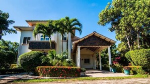 A two-story house with a covered porch and a stone pathway leading to the entrance. - Casa Trebol (Tela)