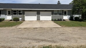 Une maison à deux étages avec une allée menant à l’entrée, deux portes de garage et un petit jardin devant la maison, agrémenté d’un arbre et de quelques arbustes.