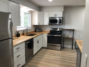 A modern kitchen with stainless steel appliances, white cabinetry, and a wooden countertop.