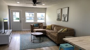 Un salon comprenant un canapé, une table basse, un meuble pour la télévision et un ventilateur de plafond.