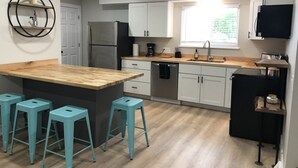 Une cuisine moderne dotée d’un îlot central, de tabourets de bar, d’appareils électroménagers en acier inoxydable et de meubles de rangement blancs.