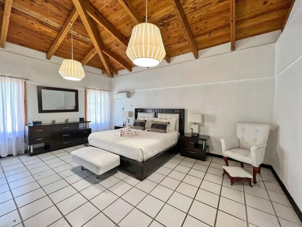 A bedroom with a large bed, a bedside table, a chair, a dresser, and a mirror.