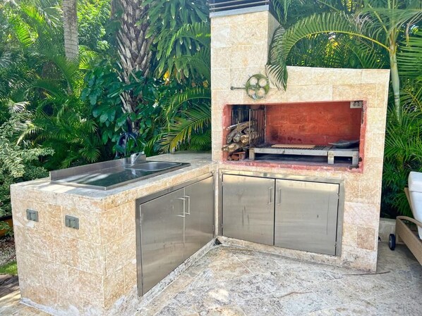 Cocina exterior con encimera de piedra, armarios de acero inoxidable y una parrilla.